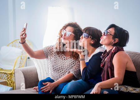 three caucasian young beautiful females doing a picture in selfie style with a mobile phone at home sit down on the sofa. friendship and connected wit Stock Photo