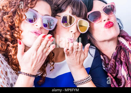 three caucasian young funny crazy woman do a party with colorful sunglasses. sending kiss and having fun together in a real friendship. group people a Stock Photo