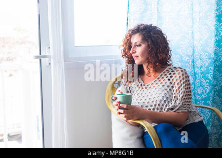 one woman at home near the window with a cup of tea or coffee. bright light and thoughts for beautiful female in a clear house. Stock Photo