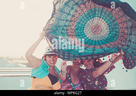 three young beautiful female ladies take a mandala textile over the heads. playing with the wind in outdoor activity. summer concept with sun backligh Stock Photo