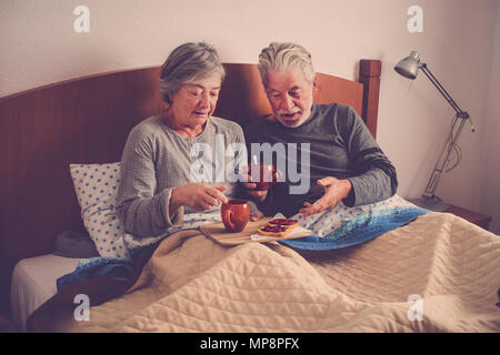 caucasian aged couple doing breakfast at home in the bed. nice natural scene at home for togheterness life concept. love and carefree people married. Stock Photo