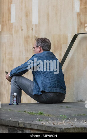 a man wearing a denim jacket sitting on some steps deep in thought and thinking. Lonliness and solitude seated alone and considering podering problem. Stock Photo