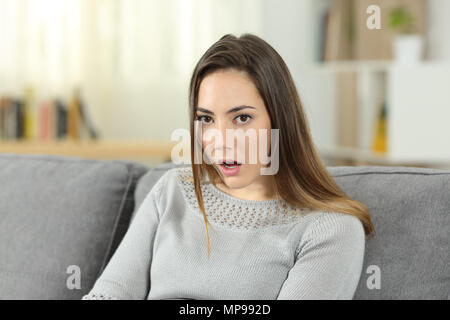 Portrait of a perplexed woman looking at camera sitting on a couch in the living room at home. She does not believe you Stock Photo