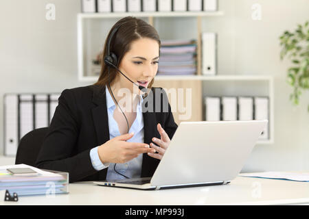 Telemarketer talking on-line having a video call with a laptop at office Stock Photo