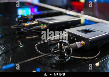Three wireless microphone transmitter and three wireless microphone reciever on black table in tv studio Stock Photo