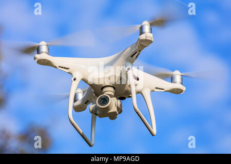 A DJI Phantom 4 Pro drone flying, blue sky in the background, selective focus on the front of the drone Stock Photo