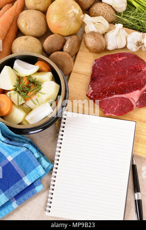 Preparing beef casserole or stew with ingredients and herbs on kitchen chopping board and blank recipe book. Stock Photo