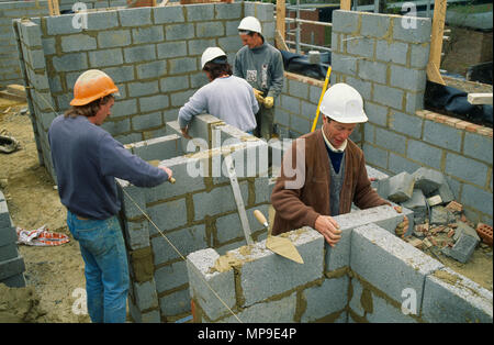 Architecture, Construction, Men working on building site wearing hard hats laying courses of concrete blocks. Stock Photo