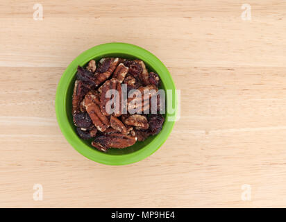 Top view of a small green bowl filled with sugar glazed pecans and dried cranberries on a wood table. Stock Photo