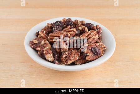 A small white bowl filled with sugar glazed pecans and dried cranberries on a wood table. Stock Photo