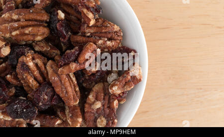 Top close view of a small white bowl filled with sugar glazed pecans and dried cranberries on a wood table. Stock Photo