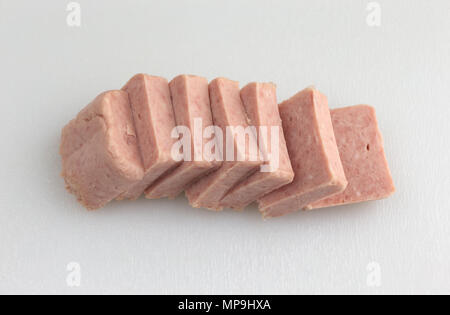 Several slices of pressed pork canned meat on a white plastic cutting board. Stock Photo