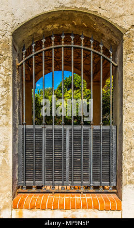 Opening in a wall secured by a grille looking into a garden, Marseille, March 2018 Stock Photo