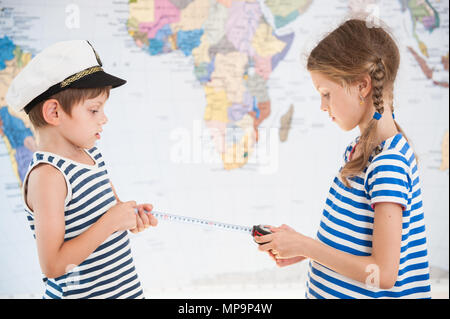 two beautiful kids in sailor striped shirts measure distance on world map with measuring tape Stock Photo