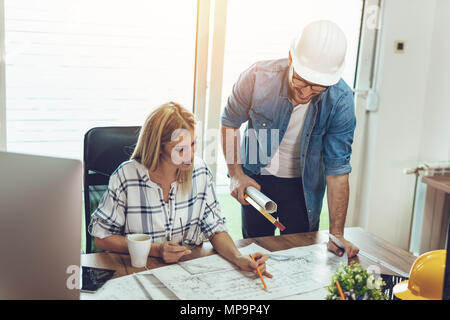 Young worried architect colleagues talking and analyzing blueprints while working on a new project at the office. Stock Photo