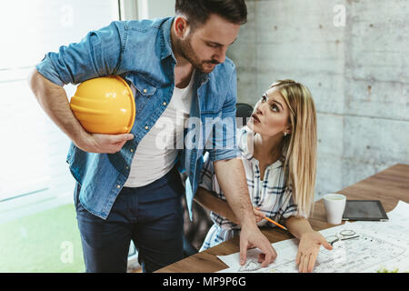 Young worried architect colleagues talking and analyzing blueprints while working on a new project at the office. Stock Photo