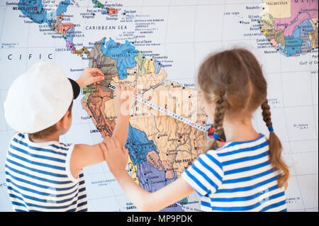 beautiful boy and a girl in sailor striped shirts measure distance on world map with measuring tape Stock Photo