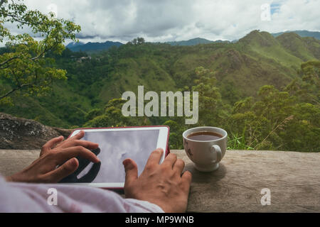 Woman using digital tablet PC sitting outdoor and drinking tea. Stock Photo