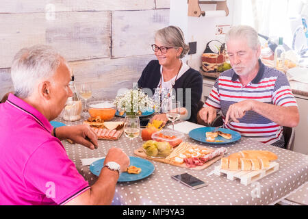 Group of senior people having lunch together at home. She smiles and other eat serious. Salami bread and vegetables on the table Stock Photo