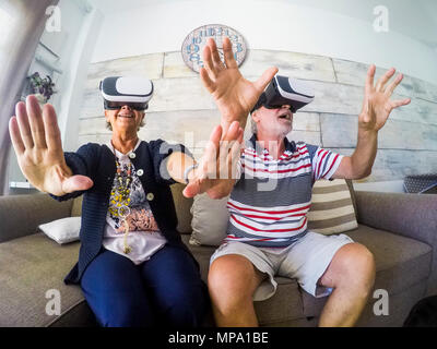 Couple of aged man and woman senior elderly play at home on the sofa with goggles headset trying virtual reality video games and vides. Activityies at Stock Photo