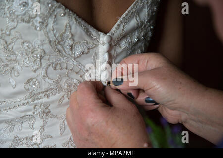 Brides dress being done up by her mother on her wedding day, close up of the buttons on the back of the wedding dress Stock Photo