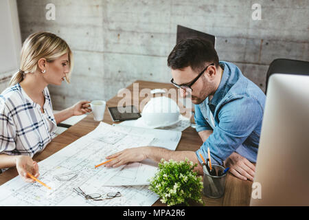 Young worried architect colleagues talking and analyzing blueprints while working on a new project at the office. Stock Photo