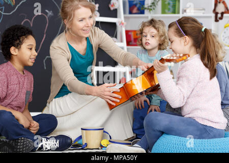 Little preschool girl holding teacher's guitar on music lesson Stock Photo