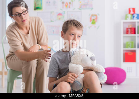 Shot of a sad boy holding a teddy bear in psychologist's office Stock Photo