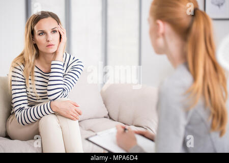 Mental health and counseling concept - psychologist listening to depressed female patient and writing down notes Stock Photo