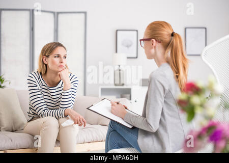 Sad thoughtful woman having a therapy session while psychologist is taking notes about her mental health Stock Photo
