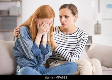 Young depressed woman crying being comforted by friend at home, girl being consoled by sister, mental problem and depression concept Stock Photo