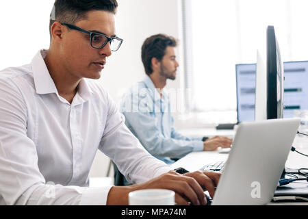 Software developers sitting at office working on computers. Man wearing spectacles working on laptop computer in office. Stock Photo