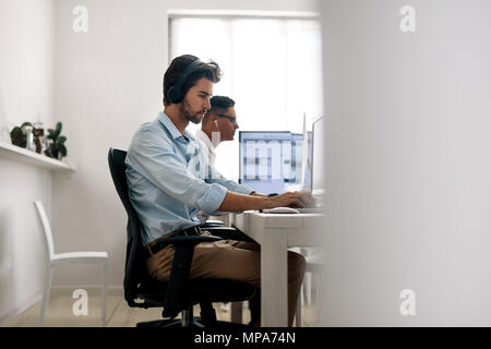 Software developers sitting at office working on computers wearing headphones. Application developer working on a laptop in office. Stock Photo