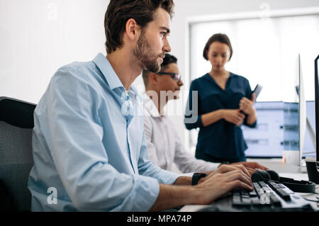 Software developers sitting at office working on computers. Two men developing applications on computer while a female colleague looks on. Stock Photo
