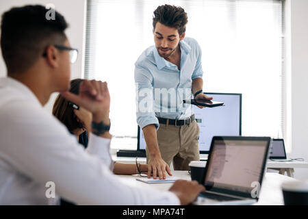 Businessman making a presentation to his colleagues in office. Office colleagues looking at laptop computers while listening to a presentation sitting Stock Photo