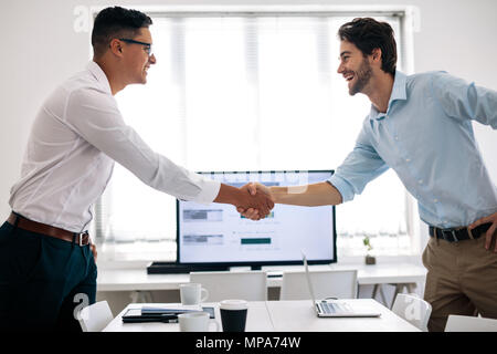 Business colleagues shaking hands in the conference table. Happy businessmen greeting each other in the meeting room. Stock Photo