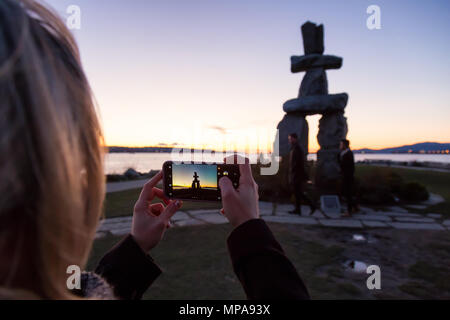 Downtown Vancouver, British Columbia, Canada - February 18, 2018: Tourist taking cell phone pictures of an Iconic Stone Sculpture, Inukshuk, on the be Stock Photo