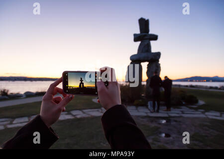 Downtown Vancouver, British Columbia, Canada - February 18, 2018: Tourist taking cell phone pictures of an Iconic Stone Sculpture, Inukshuk, on the be Stock Photo