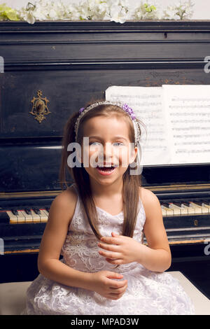 little girl in a beautiful dress near the piano happy Stock Photo