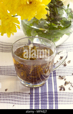 Herbal tea in glass cup and flowers on wooden table Stock Photo