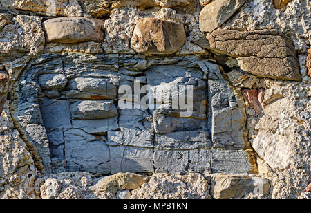 Big piece of a cracked slate in an old stone wall. Masonry construction. Rough wall, made of loose field stones and mortar without plaster. Stock Photo