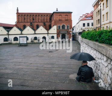 Krakow, Poland - May 23, 2017: Adult man sits with umbrella against old Synagogue in the historic Kazimierz, old jewish district in Krakow, Poland Stock Photo