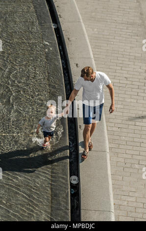 A little boy with dad walking in a fountain in a public park in Katowice, Silesian Upland, Poland. Stock Photo