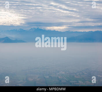 View from plane window flying South from Santiago, Chile with Andes mountain peaks and low and high level clouds in early morning Stock Photo