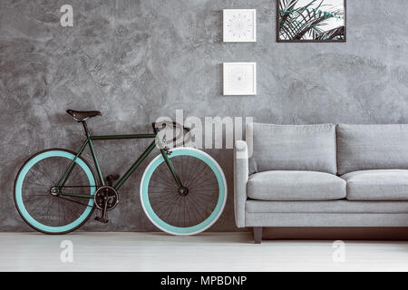 Bike with blue wheels next to grey sofa in living room with posters on concrete wall Stock Photo