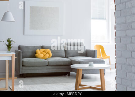 Yellow decorative pillow on grey sofa in living room with brick white wall and simple coffee table Stock Photo