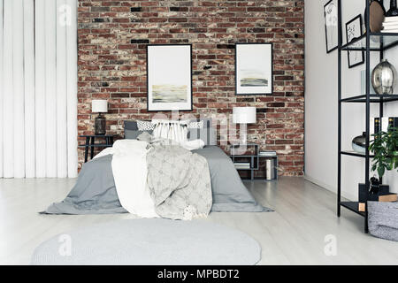 Bright bedsheets on king-size bed against brick wall with paintings in simple bedroom with lamps Stock Photo