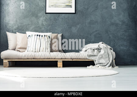 Bright mattress placed on a wooden pallet standing in bedroom with round carpet and raw grey wall Stock Photo