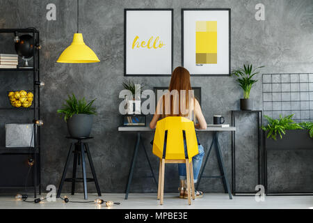 Girl sitting at her desk in posters mock-up interior with study space and modern yellow chair Stock Photo