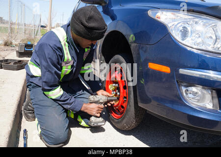 A service technician or person installing a spare tire or tyre using an impact wrench. Stock Photo